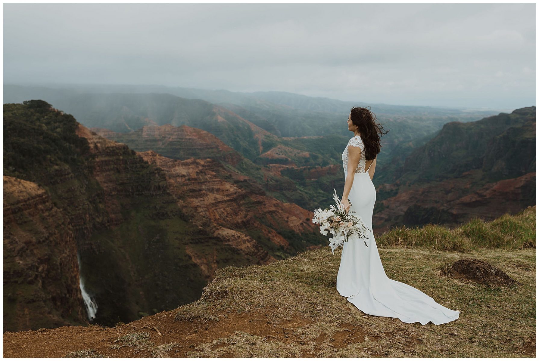 bride standing on the cliffs of Waimea Canyon in Kauai, Hawaii holding a white bouquet