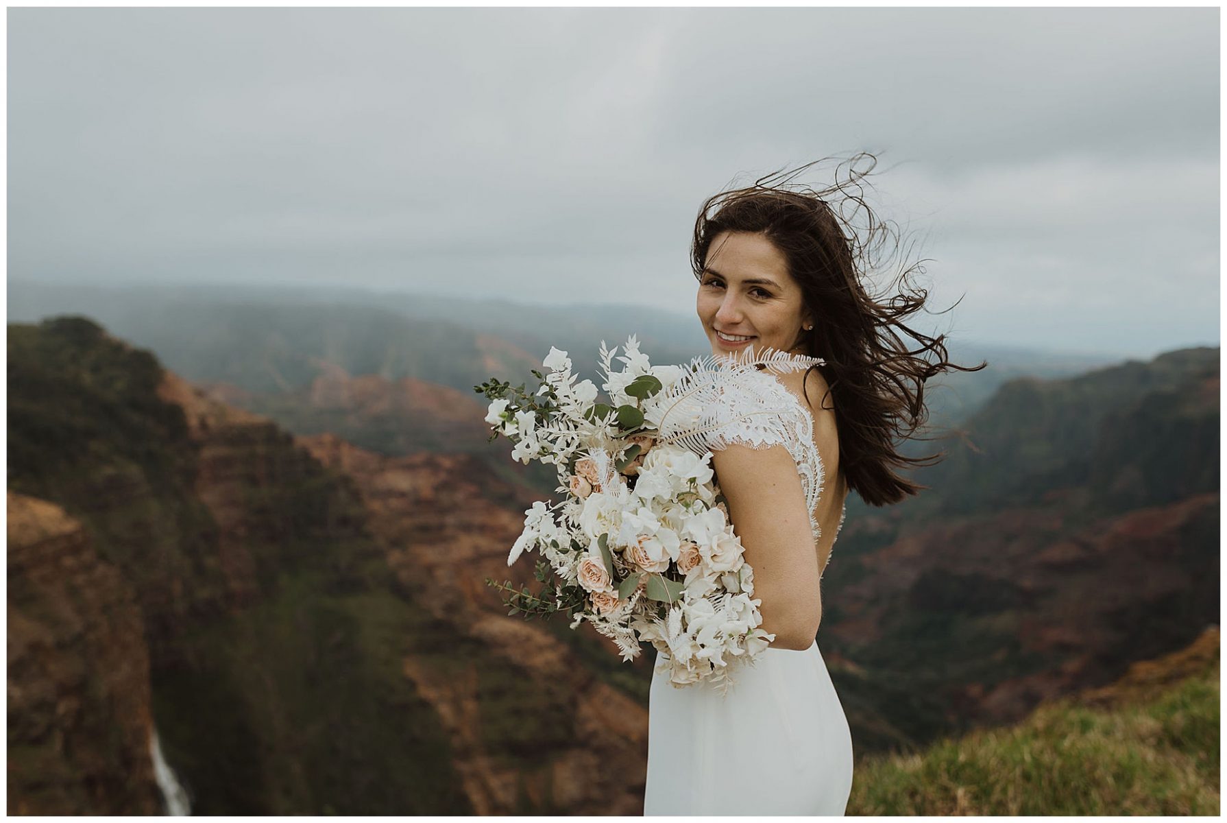 bride standing on the cliffs of Waimea Canyon in Kauai, Hawaii holding a white bouquet
