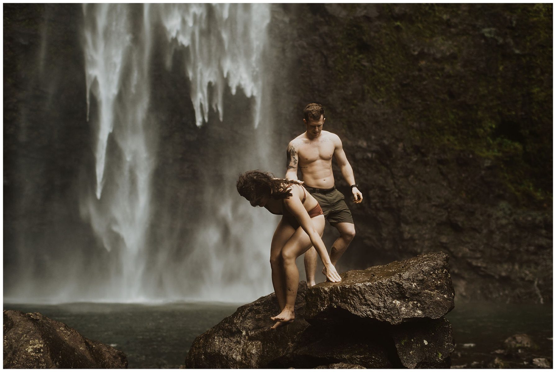 couple swimming and playing in a waterfall in kauai, hawaii