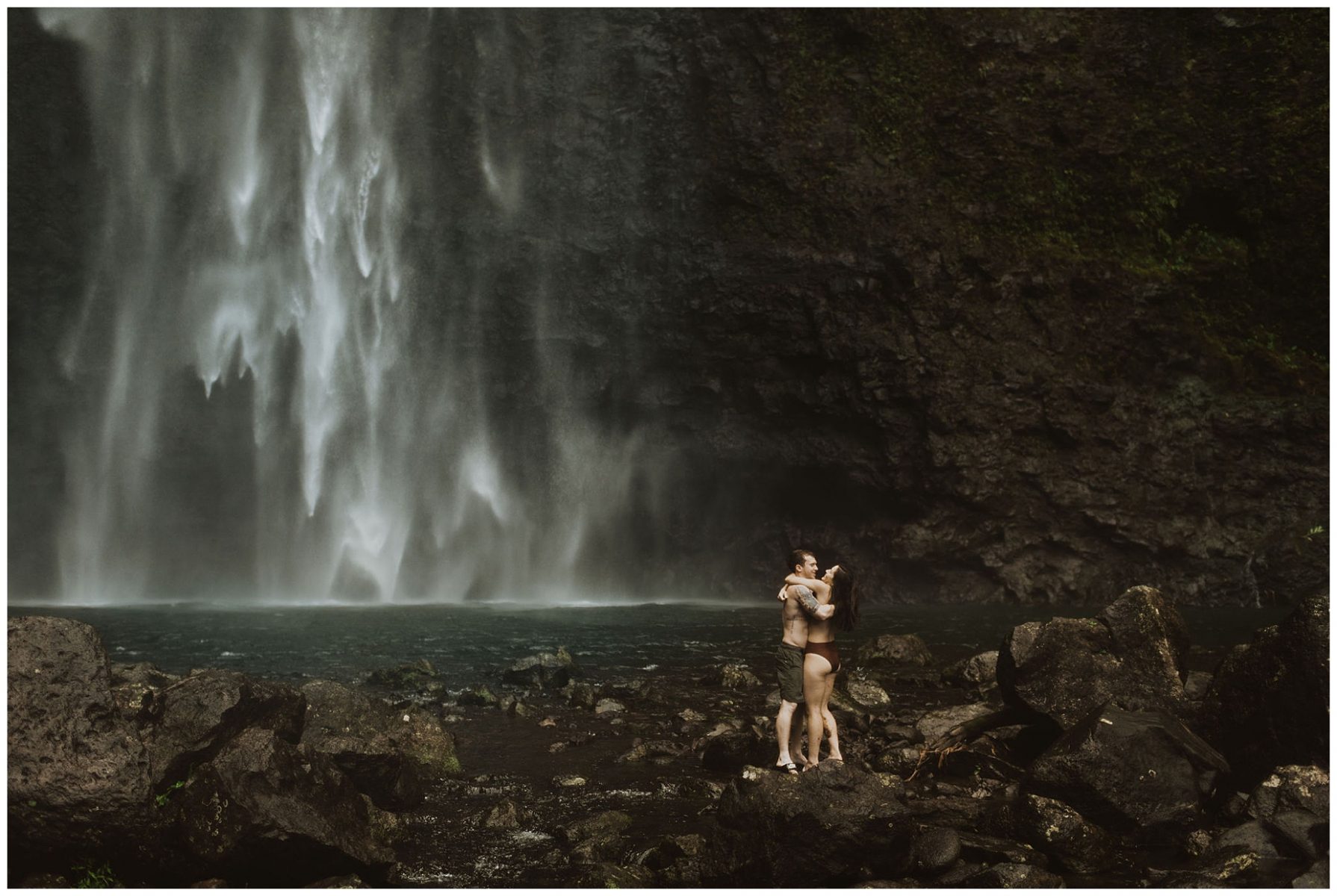 couple swimming and playing in a waterfall in kauai, hawaii