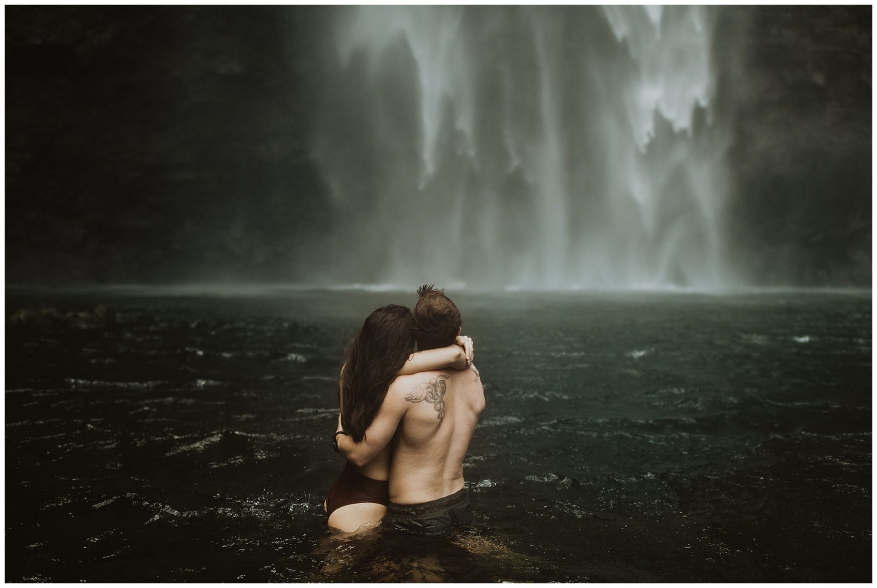 couple swimming and playing in a waterfall in kauai, hawaii