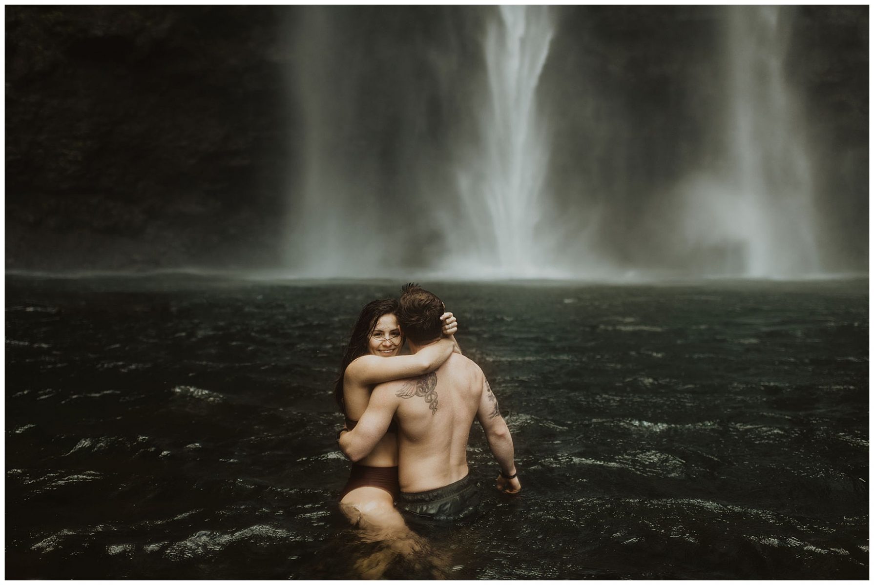 couple swimming and playing in a waterfall in kauai, hawaii