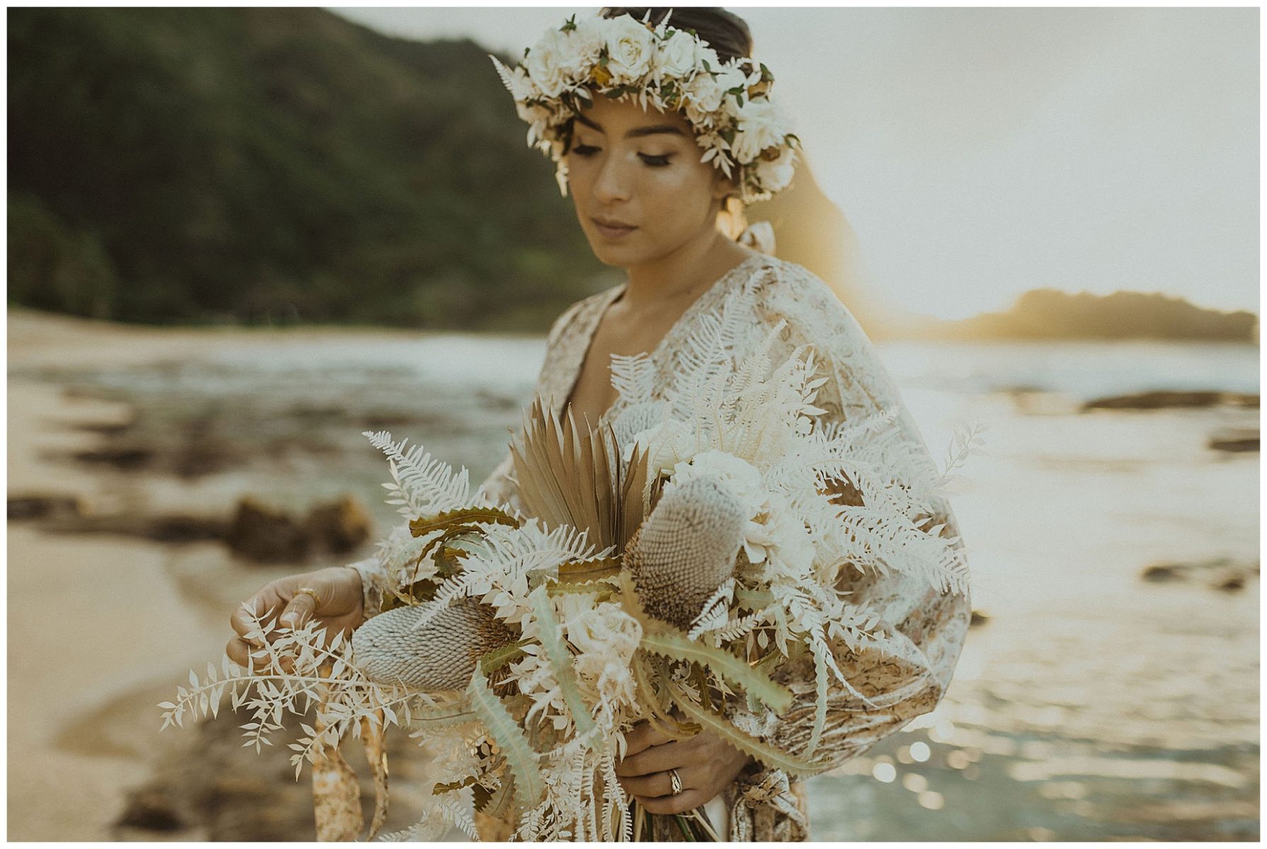 bride dressed in a gold dress holding her boho dried bouquet and wearing a white flower crown on the beach of kauai during her beach elopement in hawaii