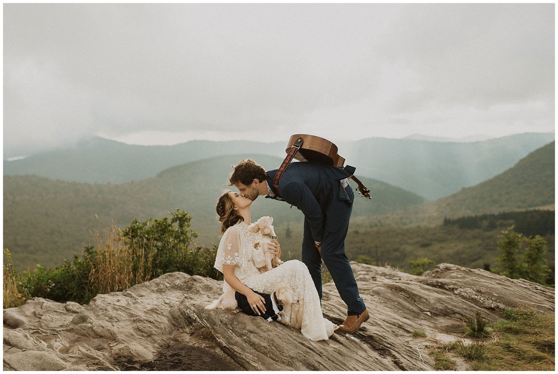 bride and groom kissing and holding their pups on top of the blue ridge mountains